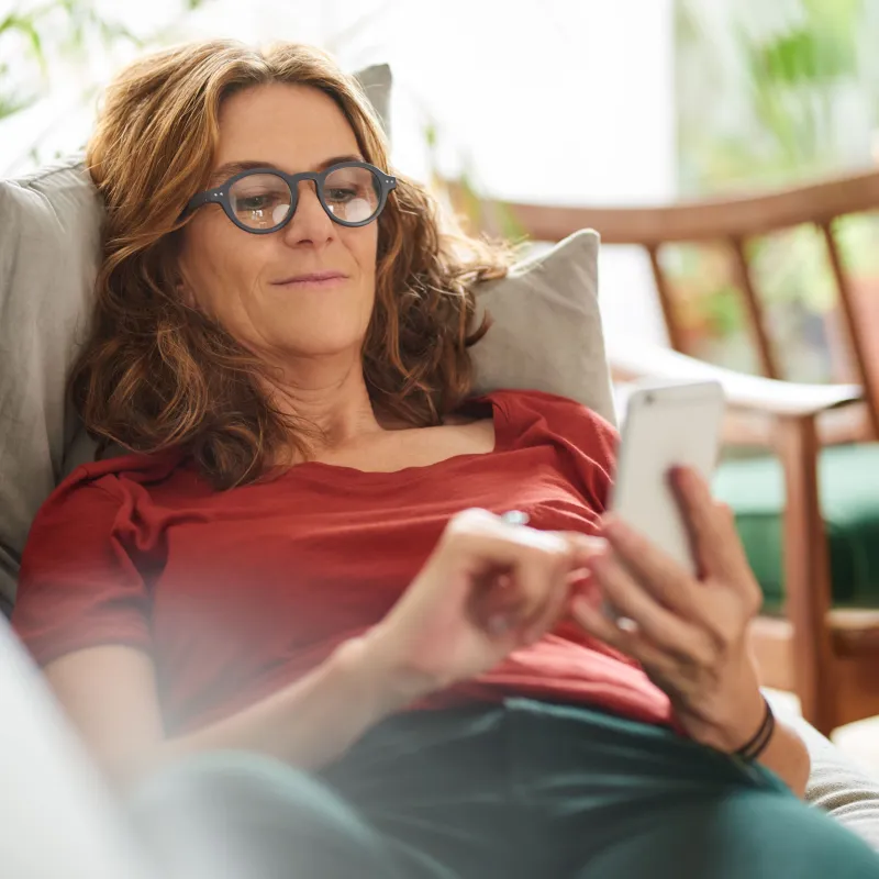 Frau liegt mit Smartphone auf Couch