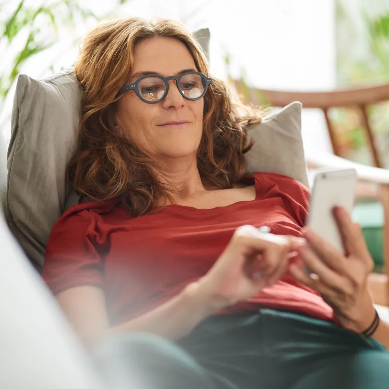 Frau liegt mit Smartphone auf Couch