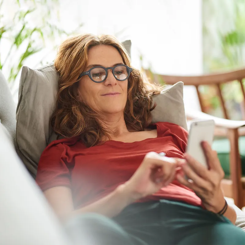 Frau mit Smartphone in der Hand auf Couch. 